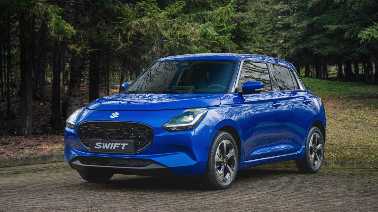 A blue Suzuki Swift parked near a forest.